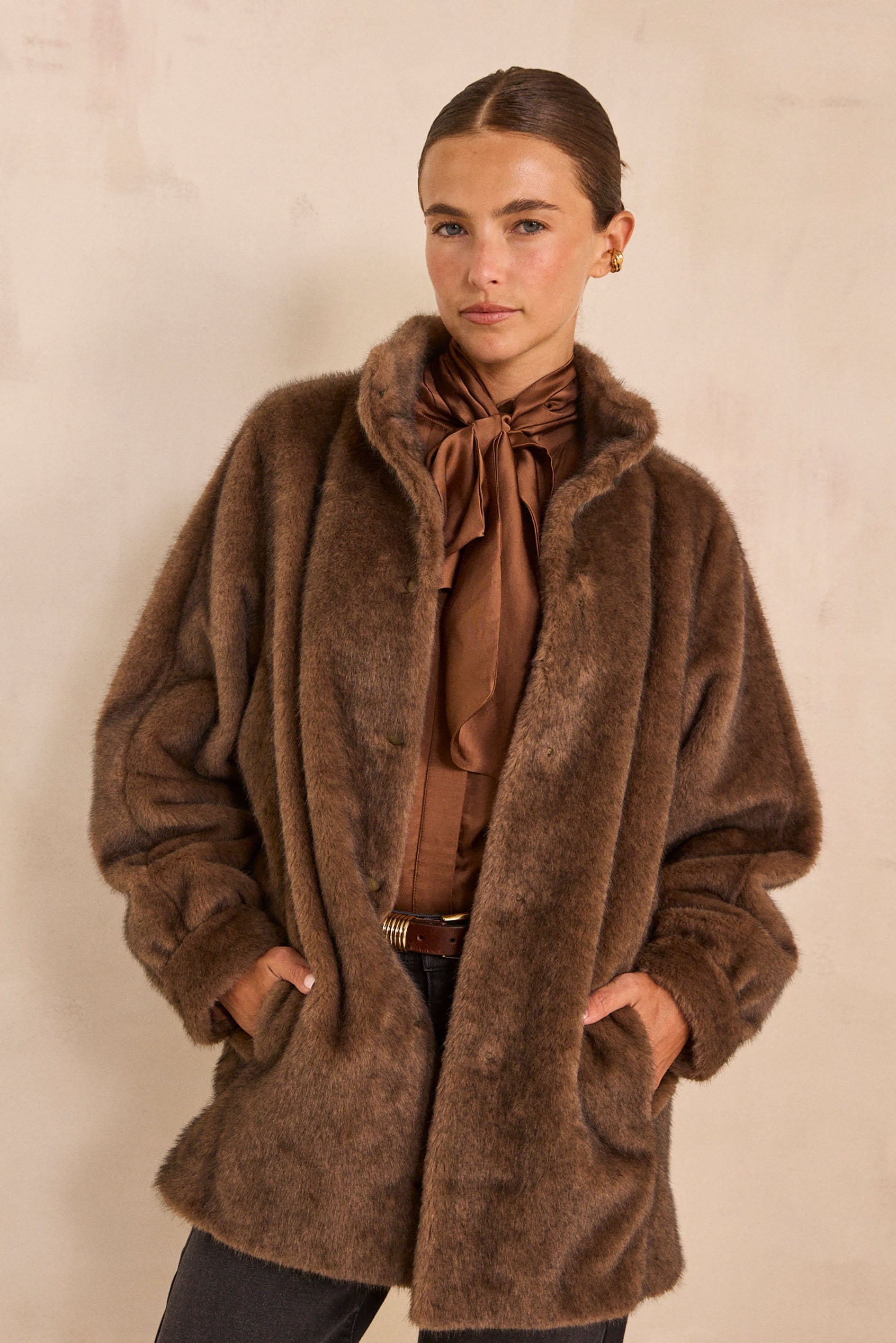 Femme portant un manteau en fausse fourrure taupe et une blouse à lavallière