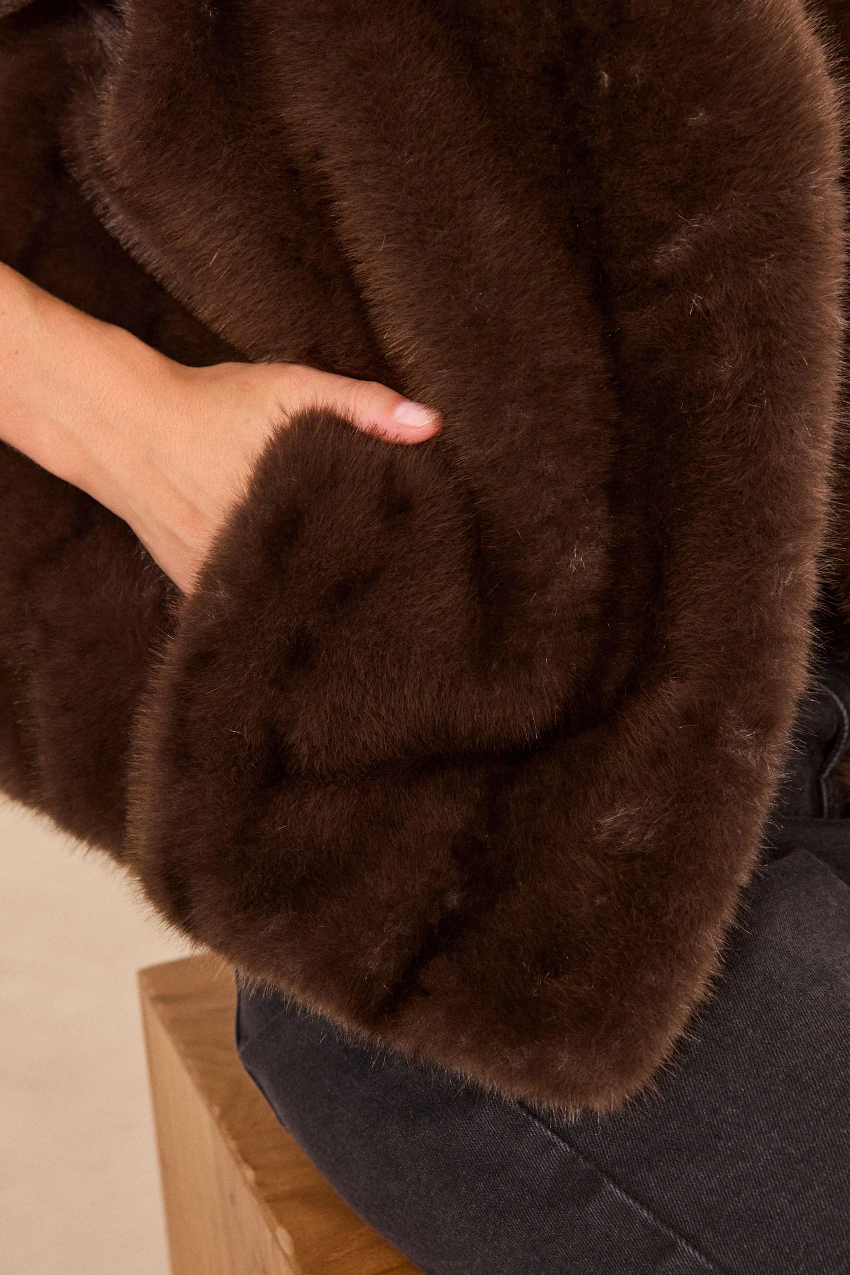 Détail d'une veste en fausse fourrure marron foncé, main dans la poche